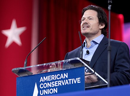 Man speaking at a podium with "American Conservative Union" text, in front of a red backdrop with a white star.