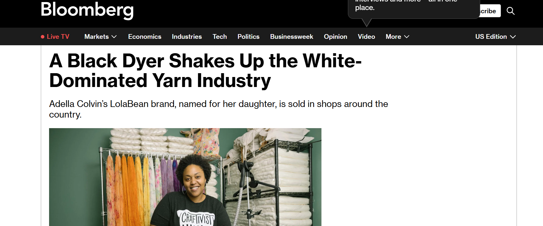 A woman stands in front of shelves of yarn, holding a basket of colorful skeins, under a sign that reads "Craftivist Creations" in a yarn shop.