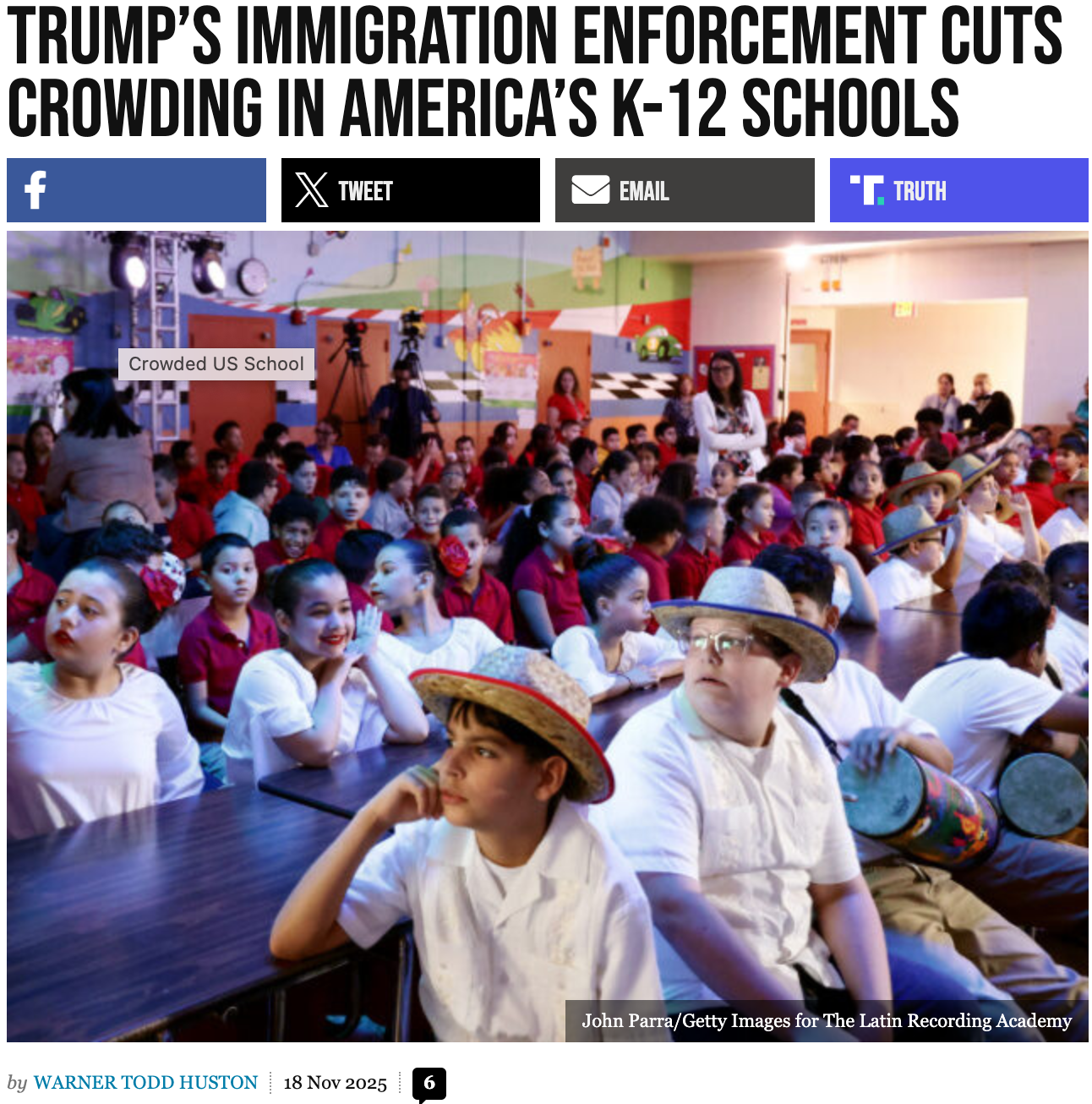 A large group of elementary school students sit closely together in a brightly decorated classroom, some wearing costumes and hats.