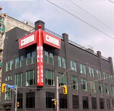 A black building with large red signs reading "CHUM" and "Dial 1050" on the corner, located at a street intersection with traffic lights.
