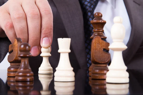 A person in a suit moves a white pawn on a chessboard surrounded by other chess pieces.