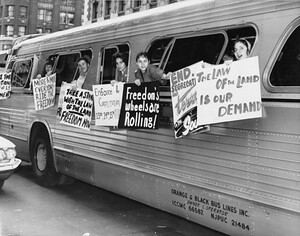 A group of people on a bus hold protest signs advocating for civil rights and desegregation in the 1960s.