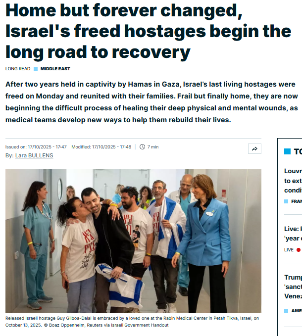 A group of freed Israeli hostages, some in hospital gowns, walk down a hallway with smiles, accompanied by medical staff and officials at a hospital in Petah Tikva, Israel.