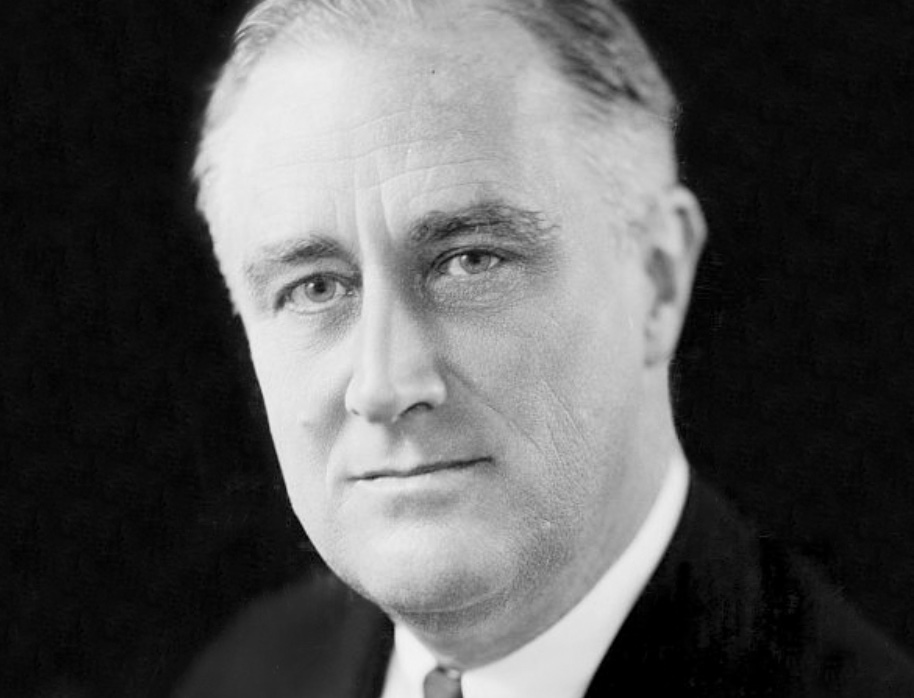 Black and white portrait of a middle-aged man with light hair, wearing a suit and tie, facing forward with a neutral expression against a dark background.