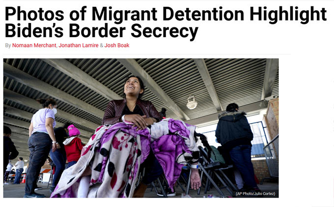 A woman sits holding a bundled blanket at a migrant detention center, with other people and cots visible under a metal canopy.