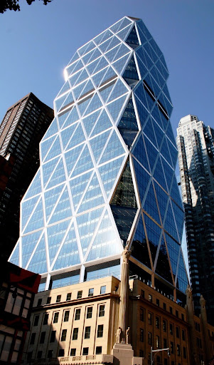 Modern glass skyscraper with a distinctive crisscross pattern on its facade, towering above older buildings under a clear blue sky.