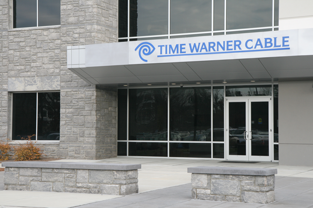 Exterior of a building with stone walls and a glass entrance displaying a "Time Warner Cable" sign above the doorway.
