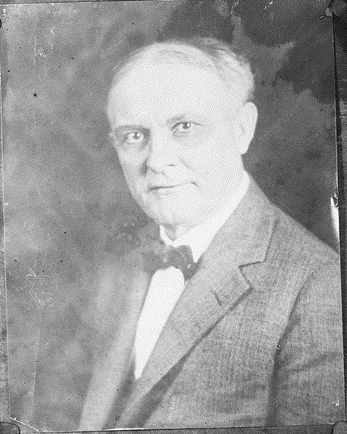 Black and white portrait of an older man in a suit and bow tie, facing the camera with a neutral expression.