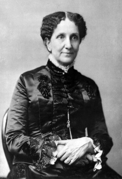 A seated woman from the 19th century wearing a dark, elegant dress with intricate detailing, looking slightly to the side.