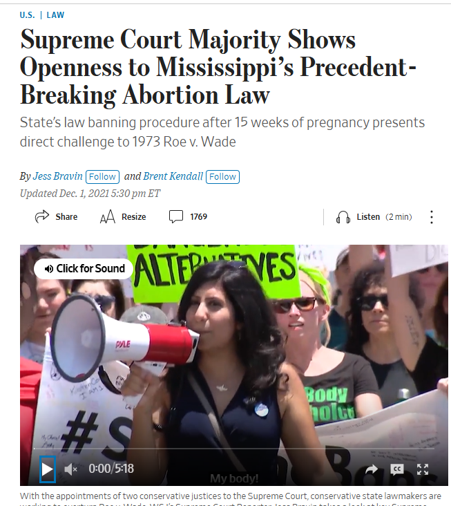 A woman speaks into a megaphone at an abortion rights protest; people around her hold signs with slogans supporting reproductive rights.