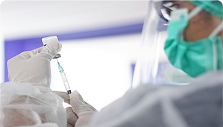 A healthcare worker in protective gear prepares a syringe with a vaccine from a vial.