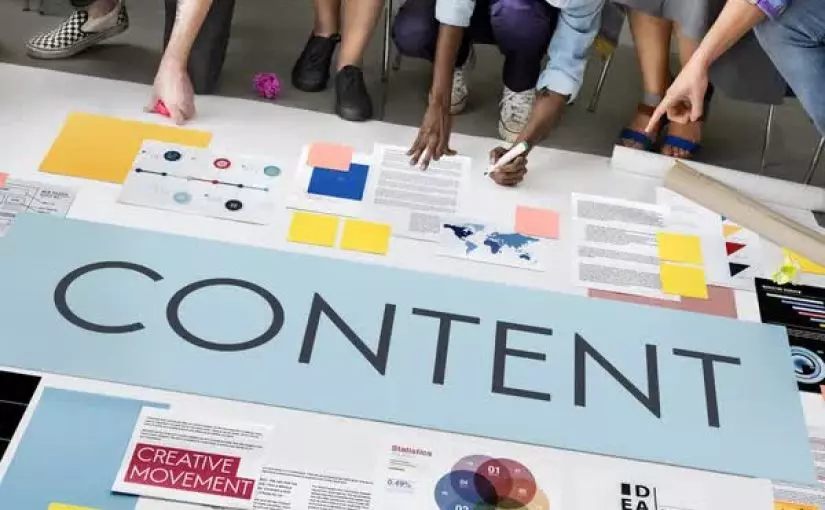 A group of people collaboratively working on a large table filled with various documents, charts, post-it notes, and a large banner that says "CONTENT.